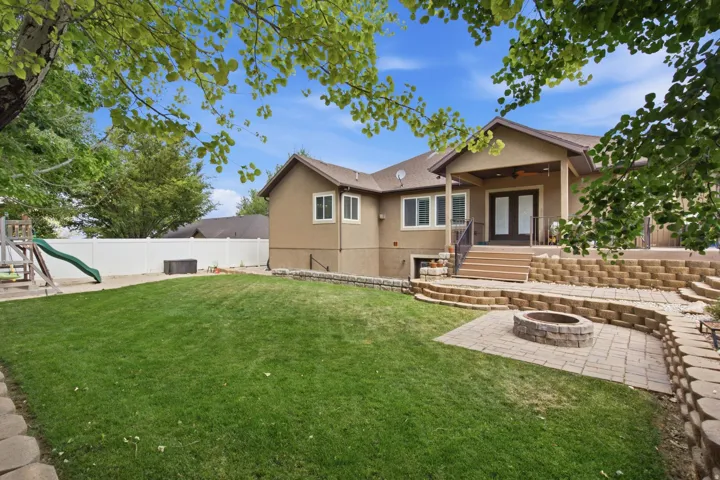 Expansive backyard featuring a tiered paver patio with a built-in fire pit, a covered outdoor living area with French doors, a lower-level walkout, and a vinyl privacy fence