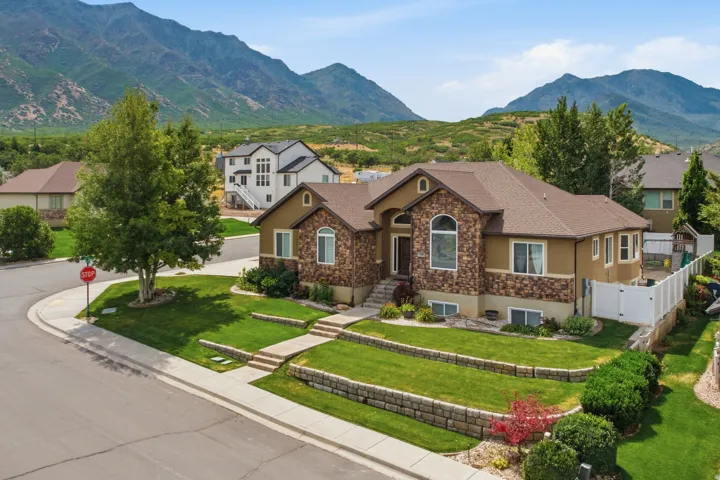 Mountain backdrop frames this residence featuring a stone and stucco exterior, arched window, tiered landscaping, paved walkways, and a side yard with white fencing