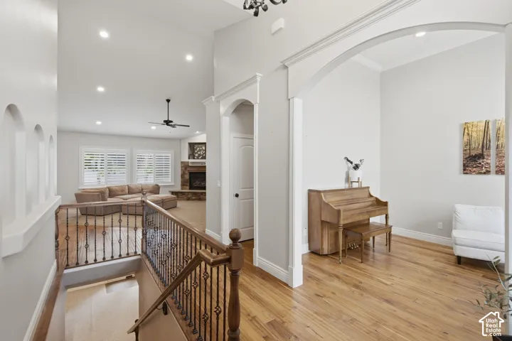 Upper-level hallway with wood-finish flooring, decorative archways, recessed lighting, and a wrought iron and wood banister overlooking the living space