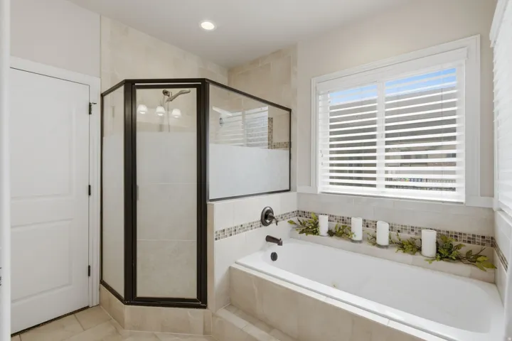 Bathroom featuring a built-in soaking tub, tile surround, and a walk-in shower with frosted glass and dark-framed enclosure