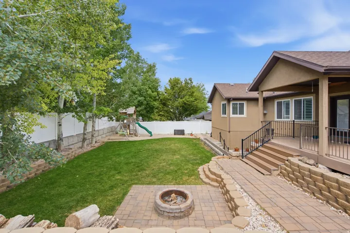 Expansive backyard featuring a paver patio with built-in fire pit, tiered landscaping with retaining walls, and a multi-level deck with stairs