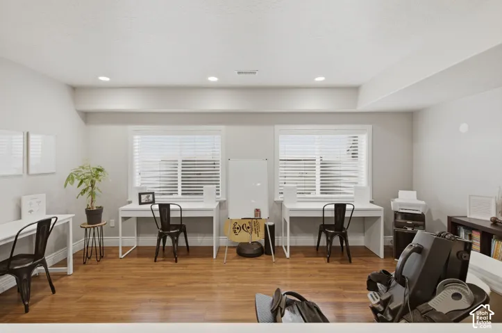 Spacious room featuring wood-finish flooring, two windows with blinds, recessed lighting, and light-toned wall finishes