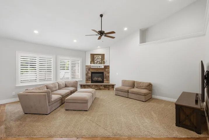 Spacious living area featuring a stone-clad fireplace with a hearth and white mantel, plantation shutters, and recessed lighting
