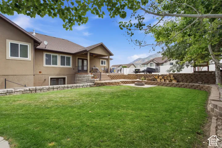 Tiered backyard featuring a covered patio, stone retaining walls, a stone fire pit area, and a manicured lawn