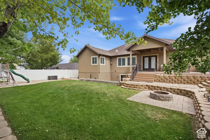 Expansive backyard featuring a tiered paver patio with a built-in fire pit, a covered outdoor living area with French doors, a lower-level walkout, and a vinyl privacy fence