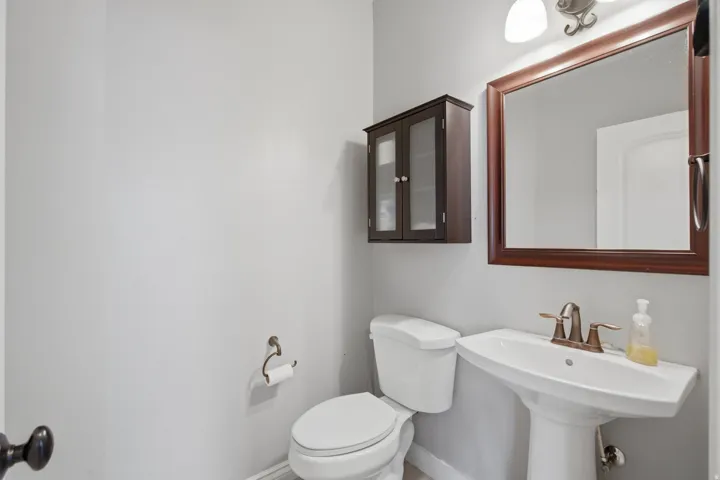 Pedestal sink with a bronze-finish faucet, framed mirror, and a wall-mounted cabinet with glass-paneled doors