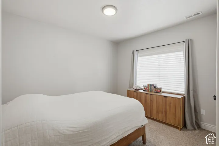 Bedroom with light gray walls, carpet flooring, and a large window with white blinds and drapes