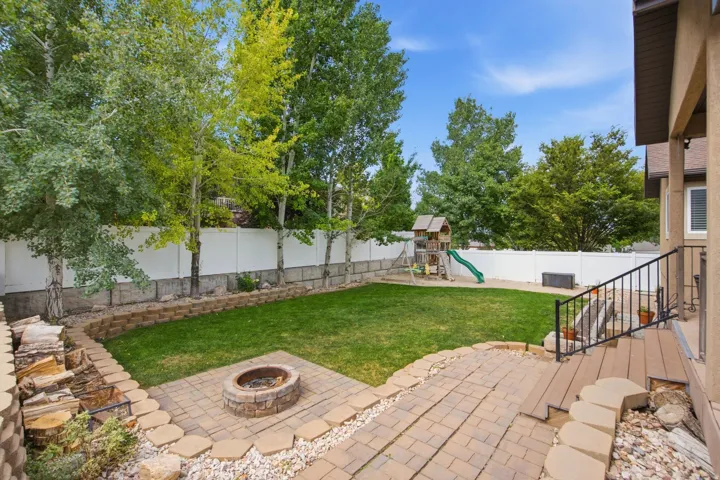 Expansive backyard featuring a lush lawn, a stone fire pit area, and a large paver patio with steps leading to the home's exterior