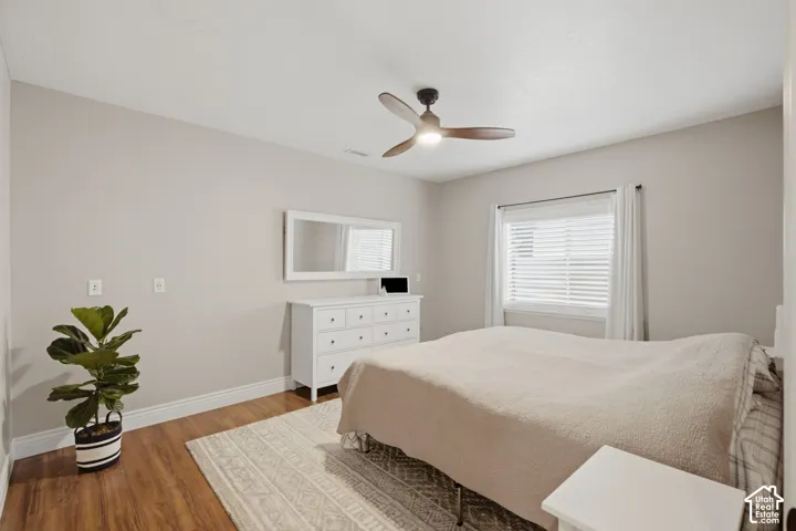 Spacious room featuring wood-finish flooring, a ceiling fan with integrated lighting, and a window with white blinds and curtains