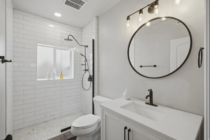 Modern bathroom featuring a walk-in shower with white subway tile, a dark-framed glass enclosure, and a built-in window