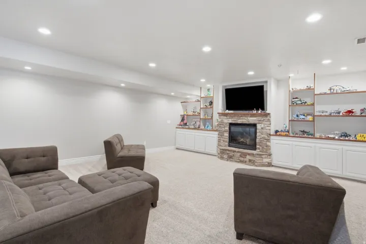 Spacious room featuring a stone-clad corner fireplace with a built-in television alcove, recessed lighting, and light-toned carpeting