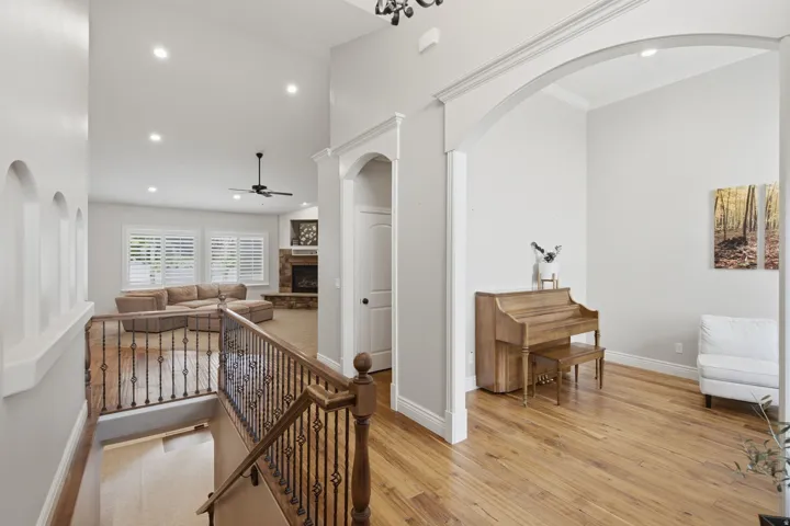 Upper-level hallway with wood-finish flooring, decorative archways, recessed lighting, and a wrought iron and wood banister overlooking the living space