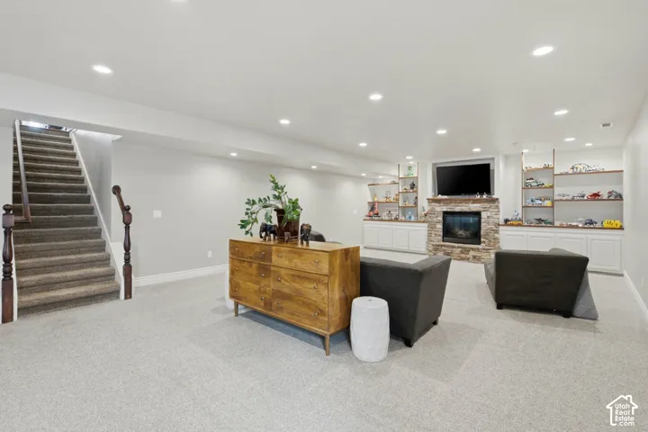 Spacious recreation room featuring light gray carpeting, a stone-clad fireplace with hearth, and recessed lighting