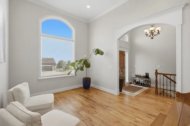 Living area featuring a large arched window with blinds, wood-finish flooring, and crown molding