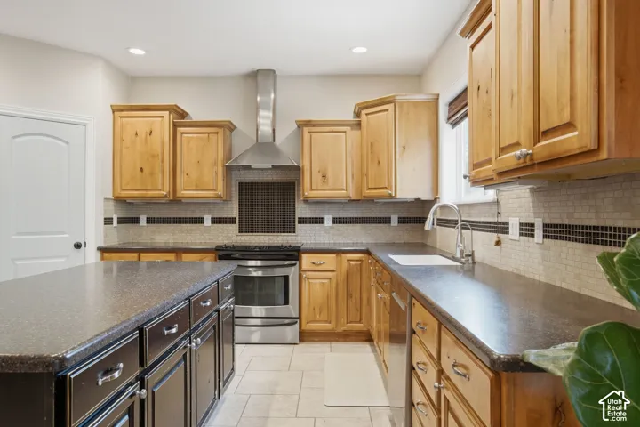 Kitchen featuring an island with dark cabinetry, light wood-finish upper and lower cabinetry, stone-look countertops, stainless steel appliances, and a mosaic tile backsplash