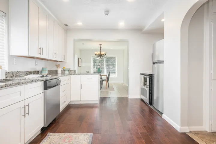 Kitchen featuring white shaker cabinetry, stainless steel appliances, speckled stone countertops, and wood-finish flooring