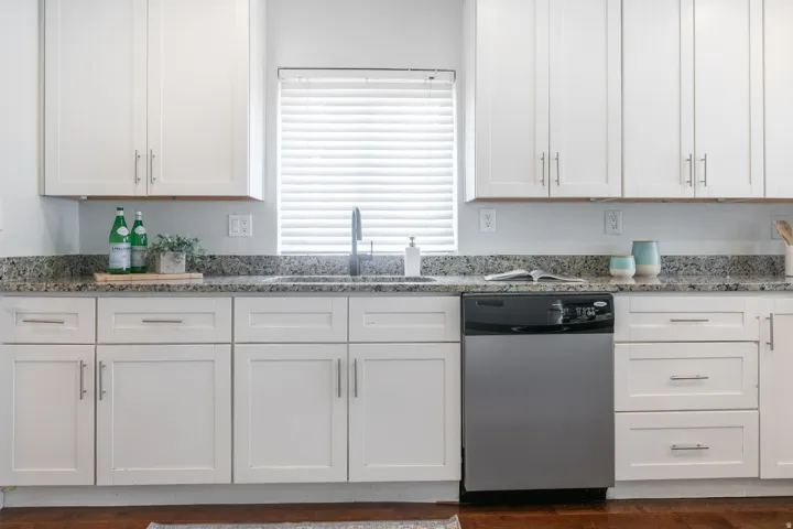 White shaker cabinetry with brushed nickel hardware, speckled countertops, stainless steel dishwasher, undermount sink, and wood-finish flooring