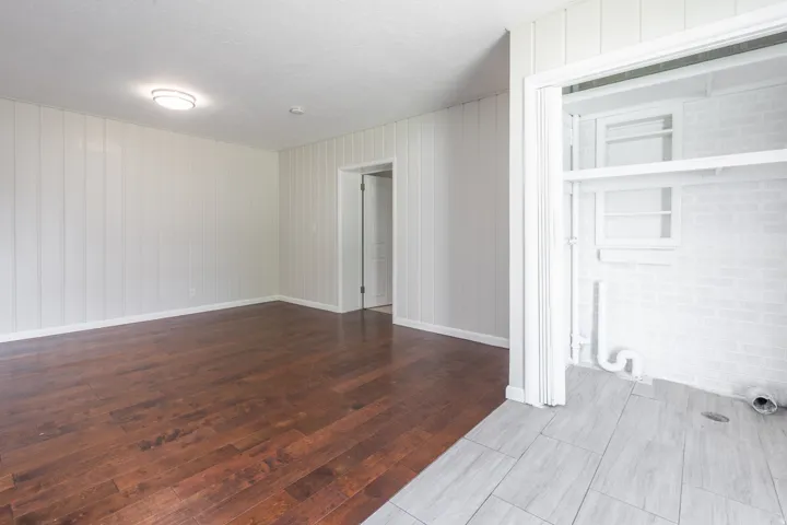 Spacious room featuring rich wood-finish flooring, vertical paneling, and a flush mount ceiling light