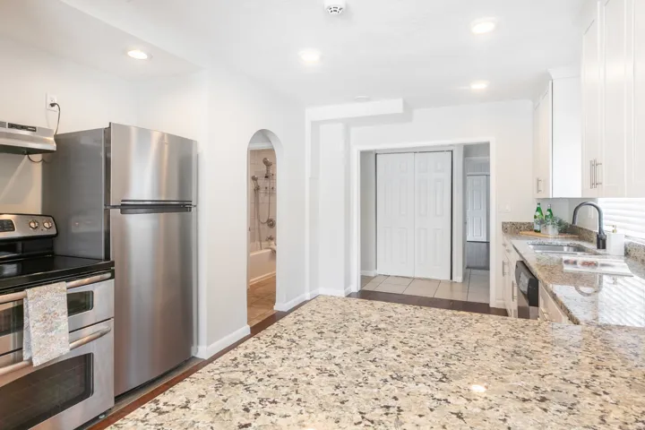 Kitchen featuring a large speckled countertop, stainless steel appliances, white cabinetry with silver hardware, and recessed lighting