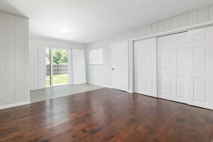 Interior space featuring rich wood-finish flooring, white paneled walls, and sliding glass doors opening to the backyard