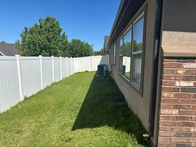Side yard with a white vinyl privacy fence, manicured lawn, and multi-pane windows