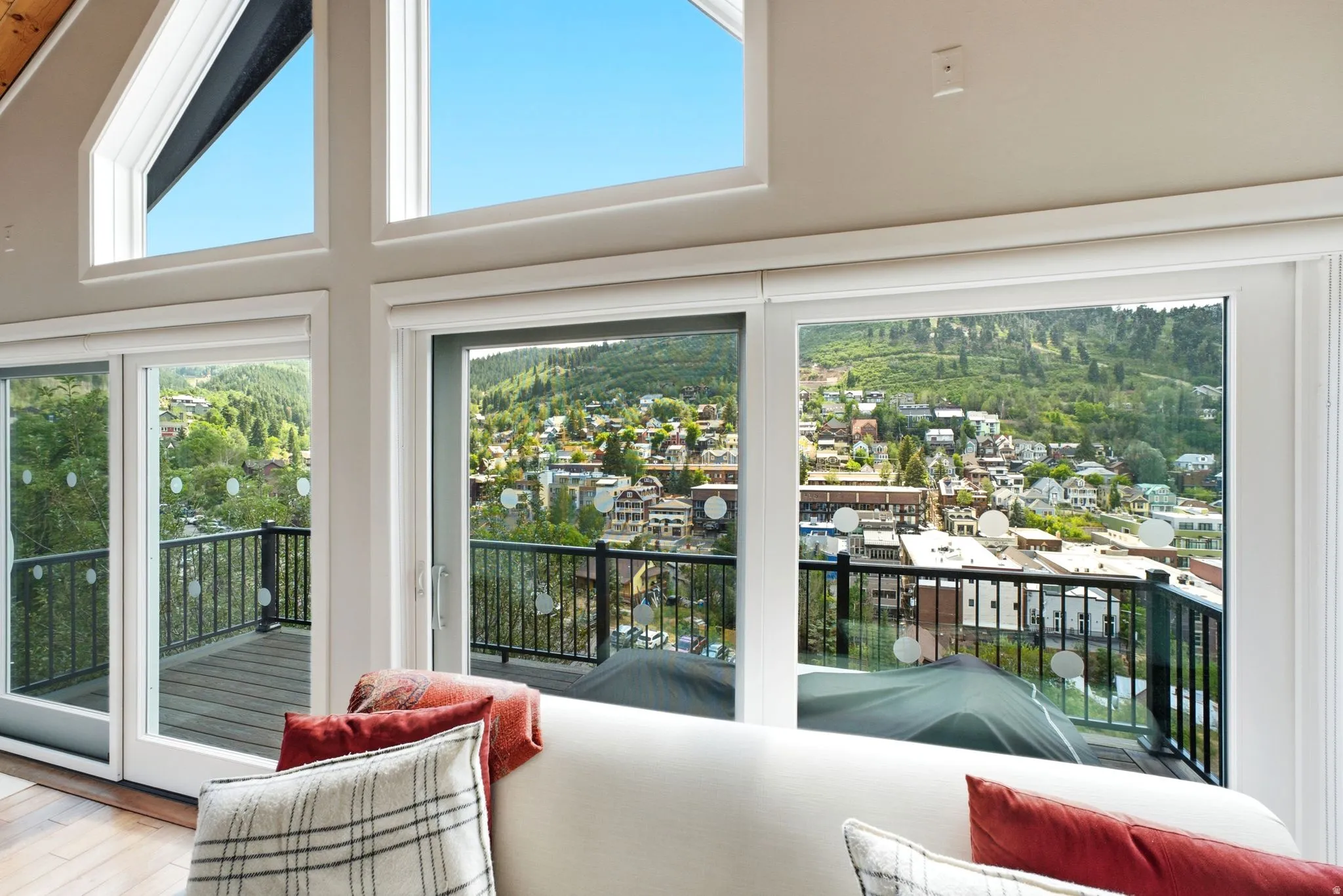 Vaulted ceilings featuring expansive windows, including transom windows, offer abundant natural light and overlook a balcony with black metal railings