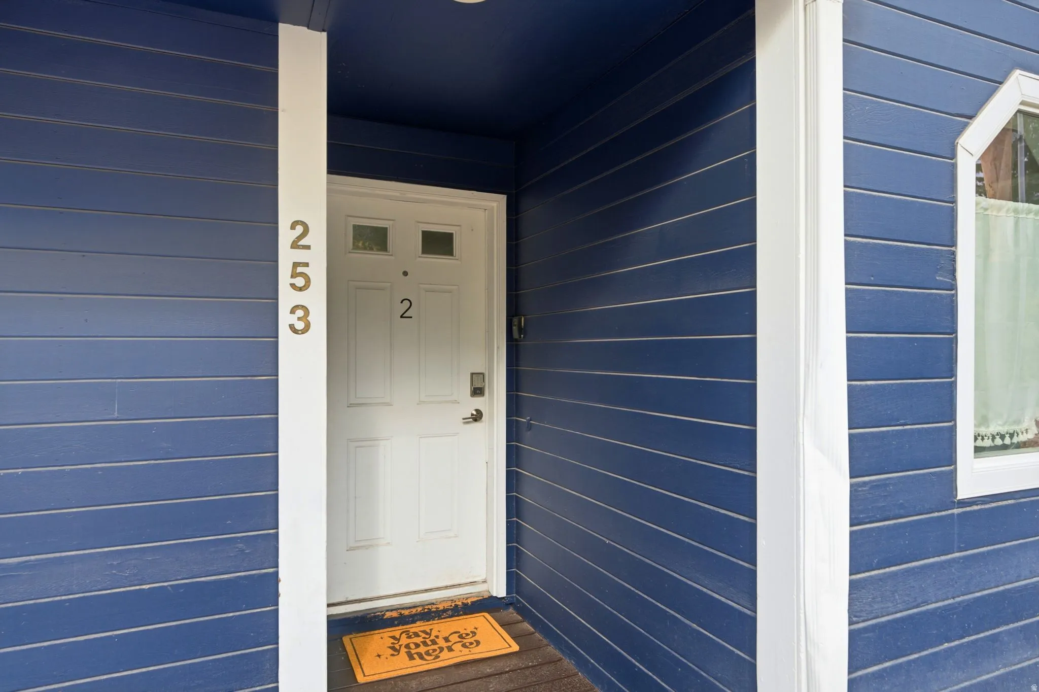 White entry door with transom windows and dark finish hardware, contrasted by blue siding and white trim