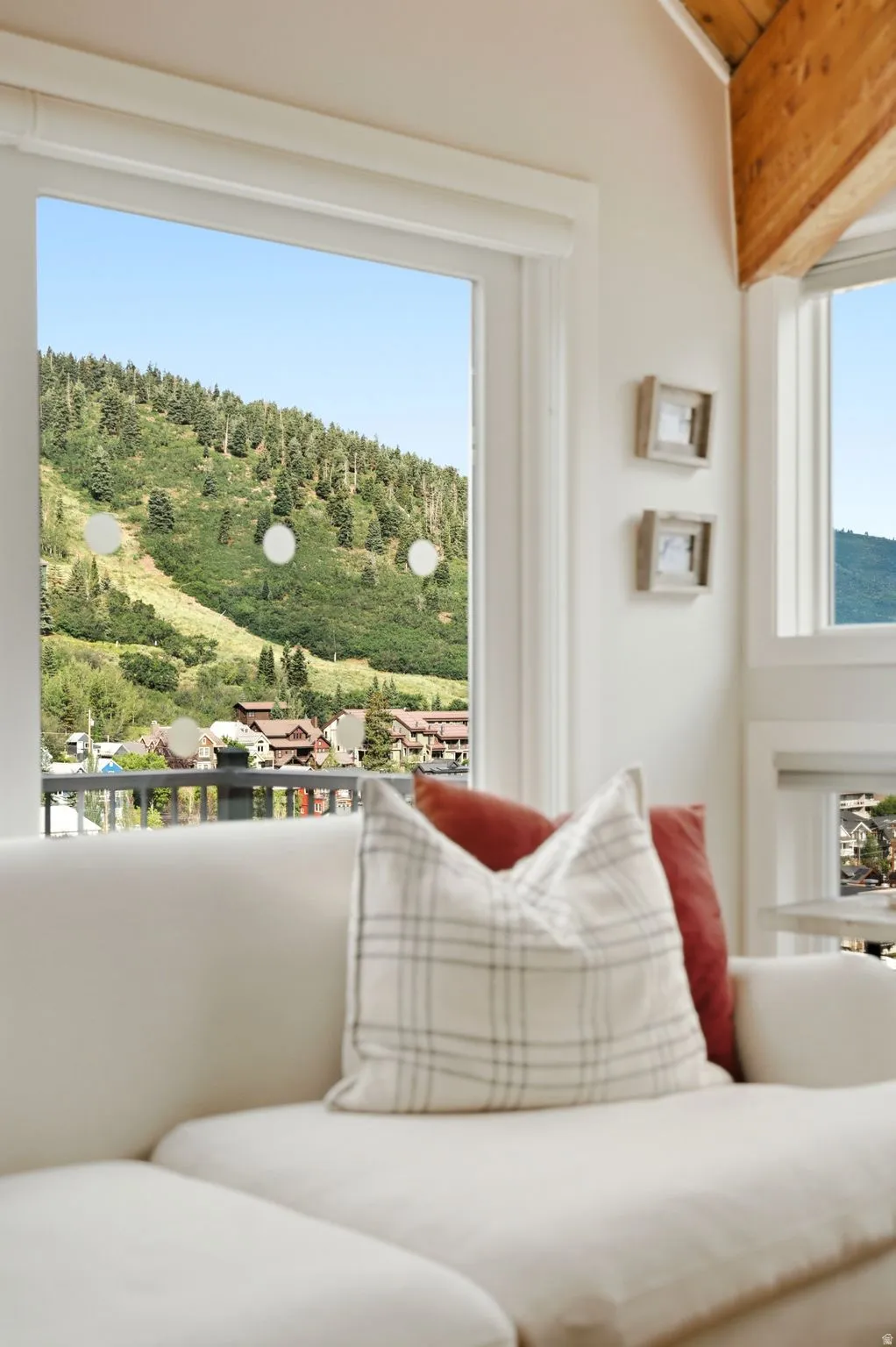 Bright interior space featuring a large window with white trim, exposed wood ceiling beams, and light-colored walls