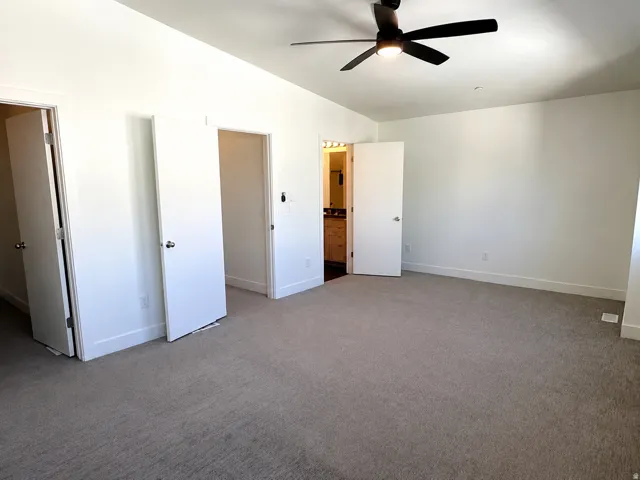 Spacious carpeted room featuring a ceiling fan with integrated lighting, white walls, and multiple doorways