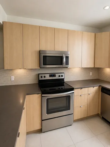 Contemporary kitchen featuring light wood-finish cabinetry, dark countertops, and a tiled backsplash