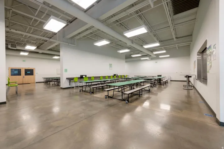 Spacious common area featuring polished concrete flooring, exposed white ceiling infrastructure, and abundant overhead rectangular lighting