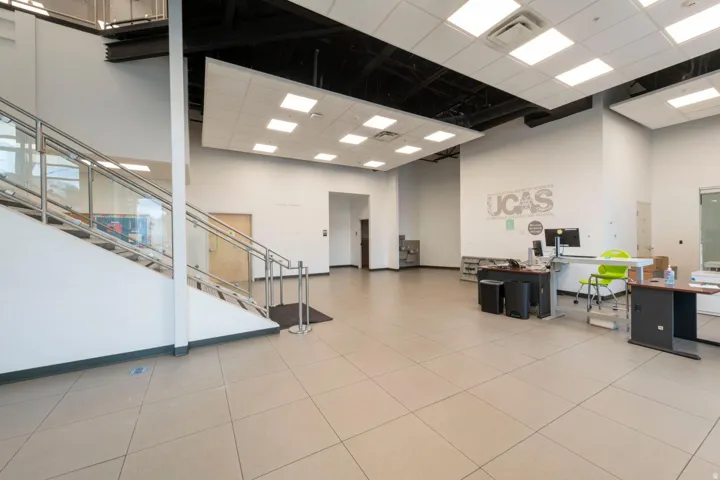Spacious open area featuring large format tile flooring, a modern staircase with glass and stainless steel railings, exposed industrial-style ceilings, and recessed lighting