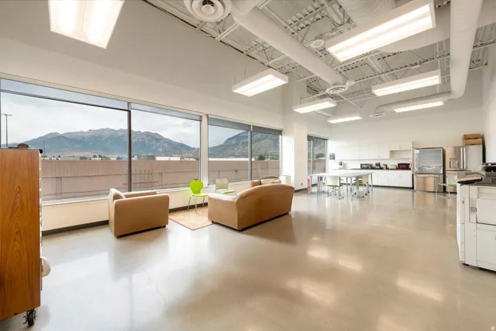 Expansive open-concept room featuring polished concrete flooring, a wall of floor-to-ceiling windows with mountain scenery, exposed ceiling ductwork, and abundant recessed and linear fluorescent lighting