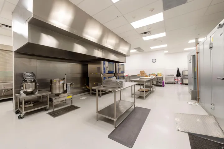 Commercial-grade kitchen featuring a large stainless steel exhaust hood, white walls, and bright overhead lighting