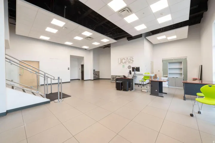 Spacious open-concept commercial interior featuring large format floor tiles, a glass and metal staircase, and an exposed ceiling with suspended acoustic panels and integrated lighting