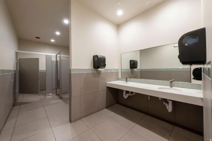 Spacious restroom featuring a dual vanity with integrated sinks, a large wall-mounted mirror, and neutral-toned wall and floor tiling