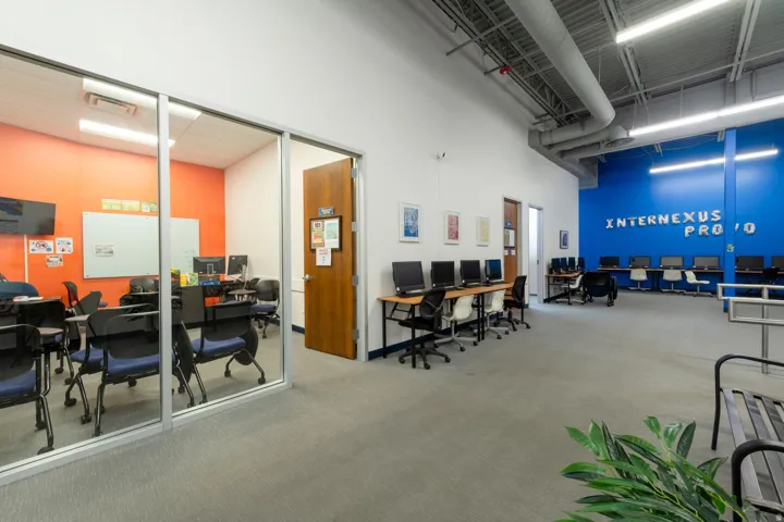 Open-concept commercial space featuring high ceilings with exposed ductwork, gray carpeting, and a vibrant blue accent wall