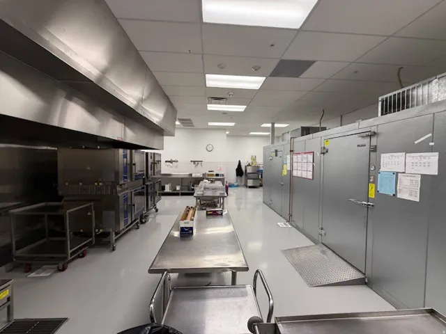 Commercial kitchen space featuring a large stainless steel ventilation hood, multiple stainless steel work surfaces, and dedicated walk-in cold storage units