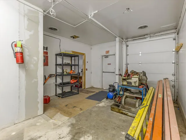 Spacious utility room featuring a roll-up garage door, concrete flooring, and an exit door