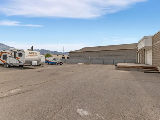 Expansive paved lot featuring a commercial building with brick-patterned block construction and a separate raised loading dock with wooden steps