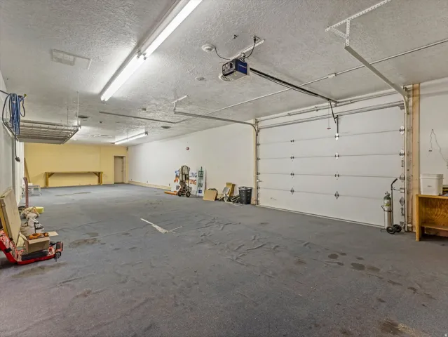 Expansive interior space featuring a large overhead door, track lighting, a textured ceiling, and an integrated workbench