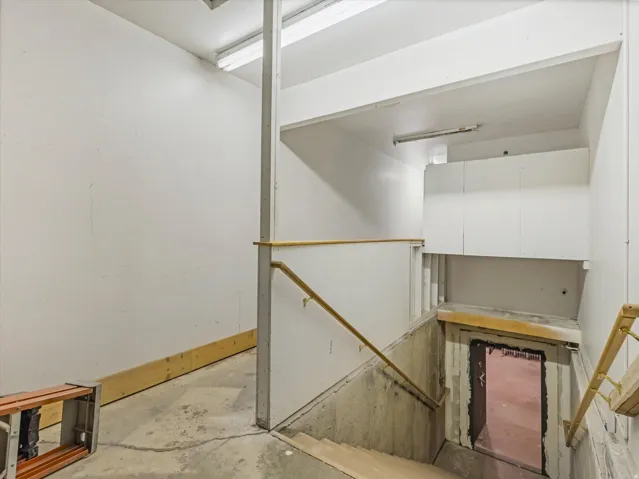 Stairwell featuring concrete steps, light wood handrails, and overhead fluorescent lighting