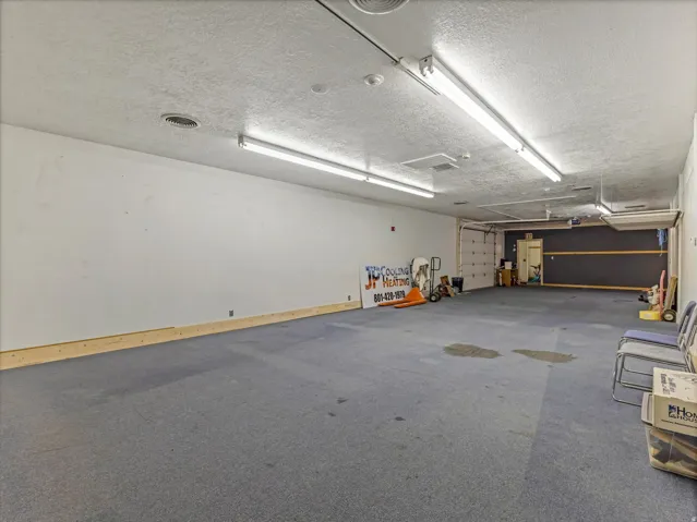 Spacious interior room with blue carpet flooring, white walls, and a textured ceiling