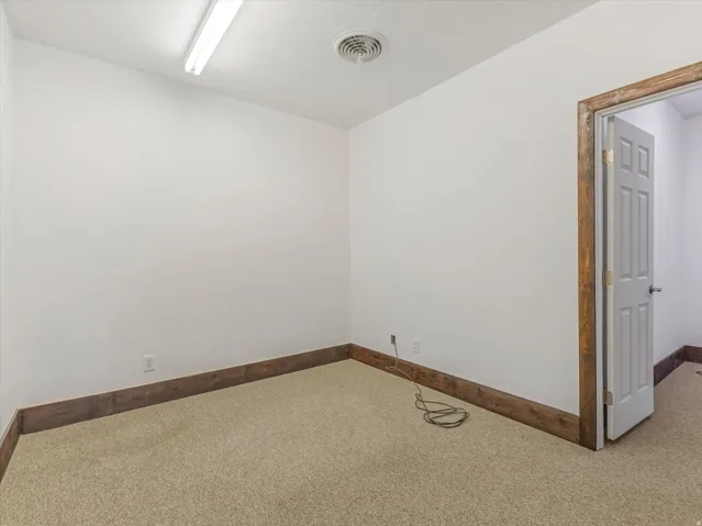 Carpeted room with white walls, wood-finish trim, and a white paneled door with wood-finish casing