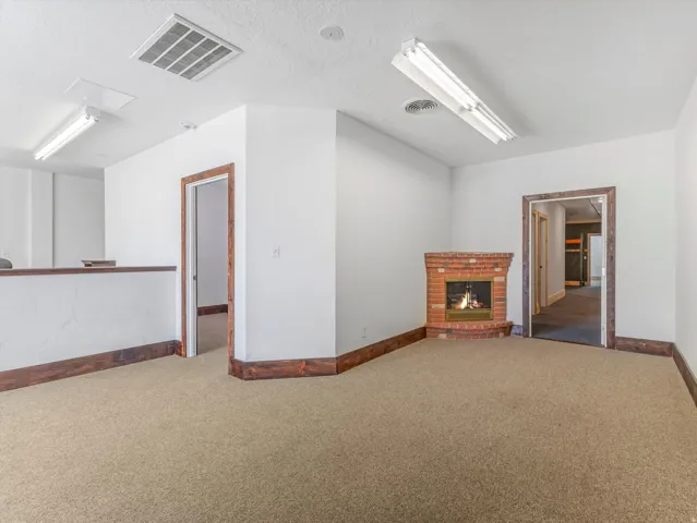Corner brick fireplace with a brass-toned insert, beige carpeting, and contrasting dark wood baseboards
