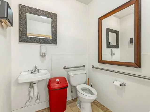 Restroom featuring a wall-mounted sink, two mirrors with contrasting frames, and grab bars