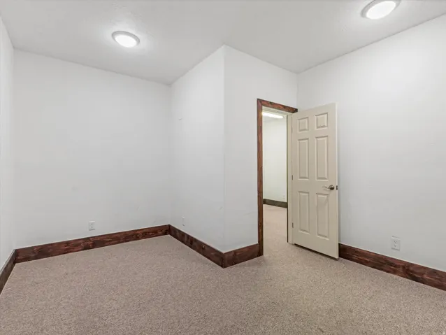 Neutral carpeted room with white walls, dark wood-finish trim, and recessed ceiling lighting
