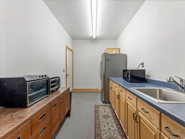 Functional utility space featuring a stainless steel sink, light wood-finish cabinetry, and blue laminate countertops