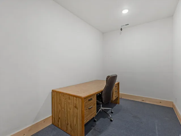 Recessed ceiling lighting illuminates a room featuring a neutral wall color, blue carpet flooring, and natural wood baseboards