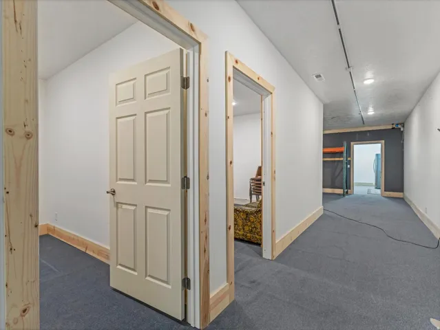 Hallway featuring light-colored walls and dark gray carpet flooring